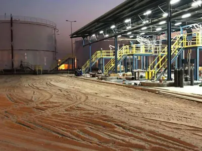 Lit loading canopy beside a storage tank at twilight