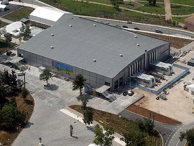 Aerial view of a large building with a grey roof, among trees