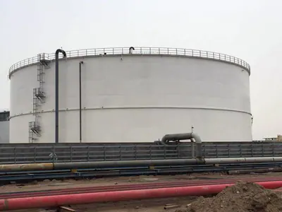 Large white storage tank with an external ladder, behind red pipes