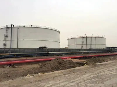 Two white storage tanks beyond red pipelines and earthworks