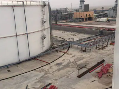 White tank shell beside a work area with stacked red pipes, industrial plant behind