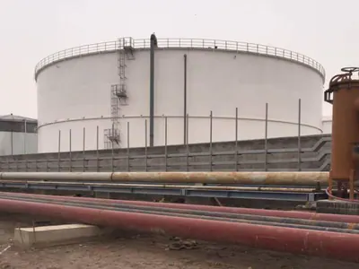White storage tank behind a row of pipelines