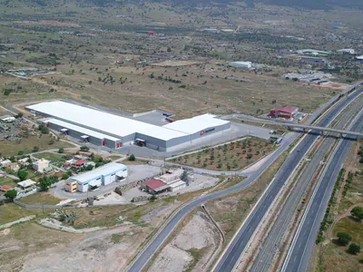 Long L-shaped logistics warehouse beside a motorway, aerial view