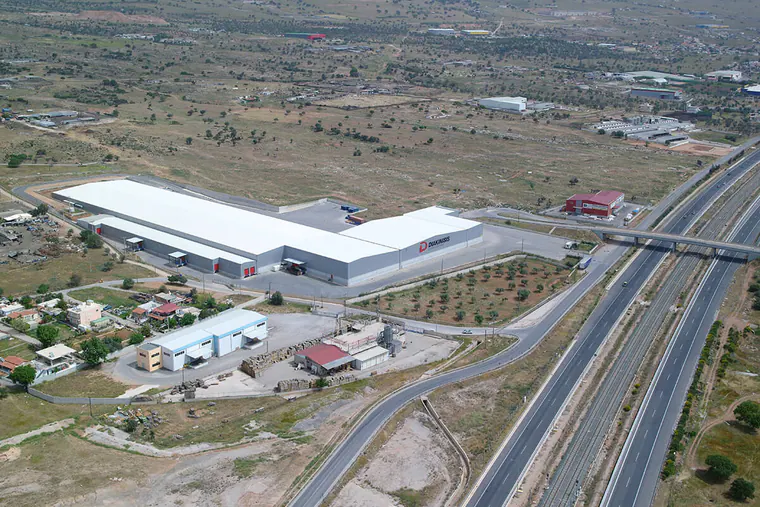 Long L-shaped logistics warehouse beside a motorway, aerial view