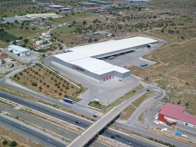 L-shaped logistics warehouse beside a motorway flyover, aerial view