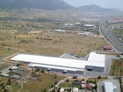 Large L-shaped warehouse in open land, with a motorway and hills behind