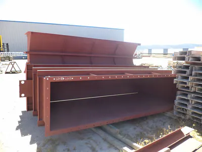 Long red-primed steel duct sections with flanges, lined up in a fabrication yard