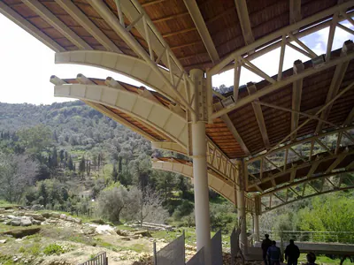 Shelter roof on round steel columns, with curved beams and lattice trusses, over an excavation