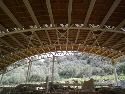 Long arched shelter over the excavation, with wooded hills beyond