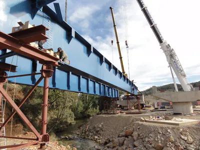 Blue bridge girders on temporary supports, with two mobile cranes