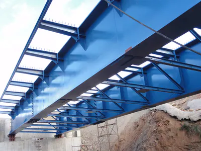 Underside of a blue steel bridge with diagonal bracing between the girders
