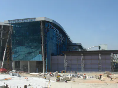 Glass-clad building under construction, with works in the forecourt