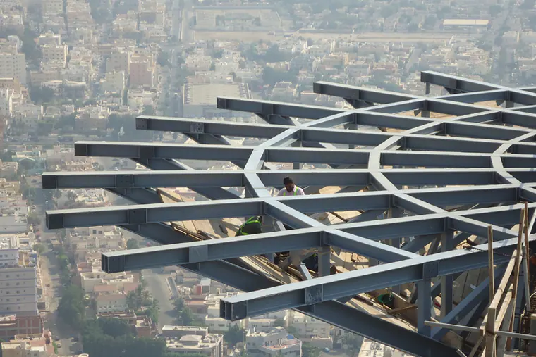 Radial steel frame with workers, high above a city
