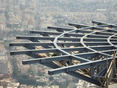 Radial steel frame with workers, high above a city