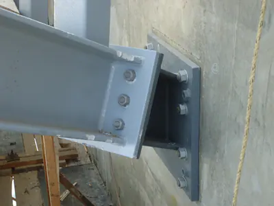 Steel beam end bolted to a bracket on a steel plate anchored to a concrete wall