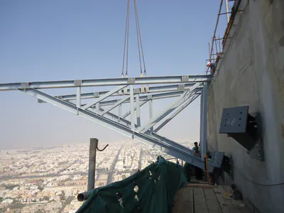 Steel truss lifted into place beside a tower's concrete wall