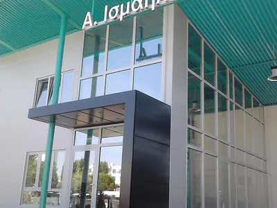 Glazed entrance under a teal steel canopy with the sign “Α. Ισμαήλος Α.Ε.”