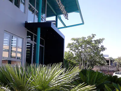 Building facade with a teal canopy, behind palm plants