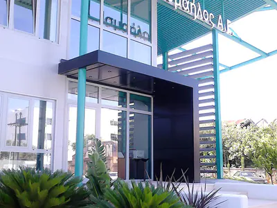 Building facade with the sign “Α. Ισμαήλος Α.Ε.” on a teal canopy and a planted garden in front