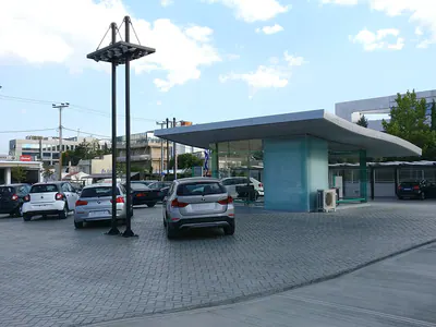 Flat-roofed pavilion and lighting masts over a paved car park