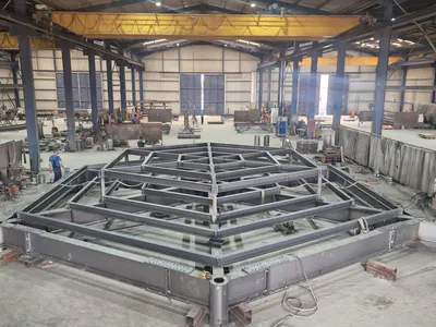 Large polygonal steel frame assembled on the floor of a production hall, rings of beams rising to its centre