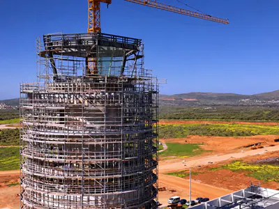 Top of a round tower wrapped in scaffolding, with a glazed cab and a tower crane's jib above