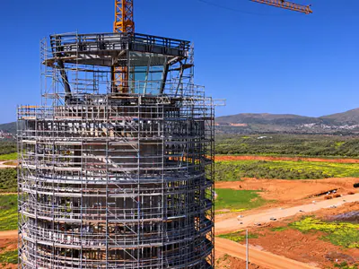 Scaffolded top of a round tower with a glazed cab, fields and hills behind