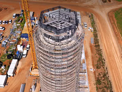 Round tower in scaffolding seen from above, its many-sided roof frame open, a tower crane and site cabins beside it
