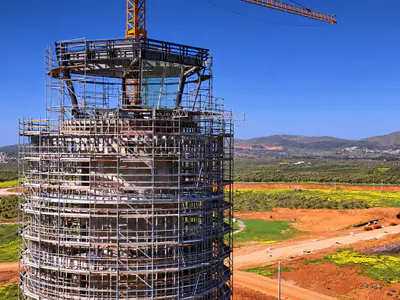 Close view of a tower's scaffolded top with a glazed cab and a crane jib, fields behind