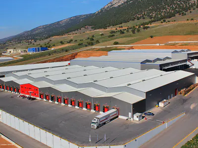 Large warehouse with a row of red loading doors and trucks, aerial view