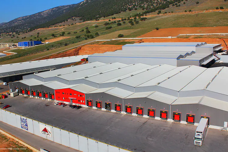 Long warehouse with red loading doors beside a boundary wall