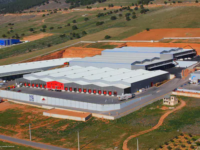 Warehouse complex with red loading doors among fields, aerial view