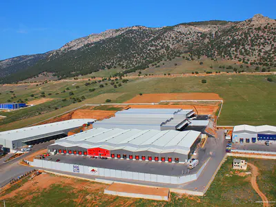 Warehouse complex in a valley below mountains, aerial view