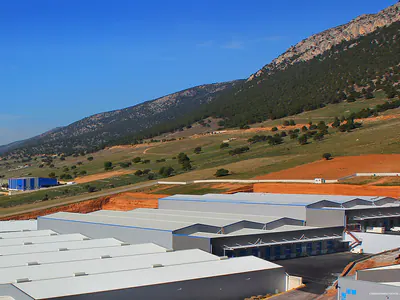 Warehouse roofs below a wooded mountainside, seen from above
