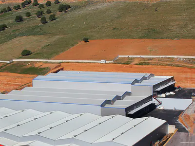 Rows of warehouse roofs with loading bays, next to bare red earth