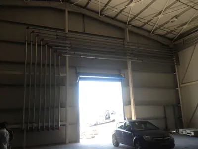 Warehouse hall with an open door and vertical pipework along the wall