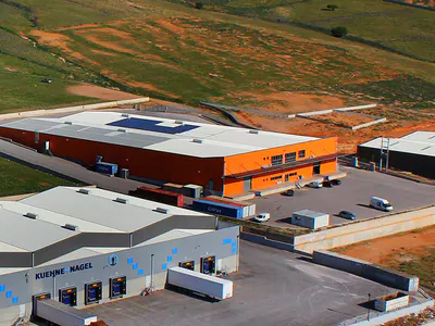 Warehouse buildings with loading bays beside a hillside, aerial view