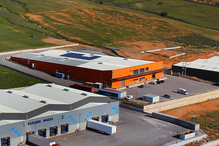 Warehouse buildings with loading bays beside a hillside, aerial view