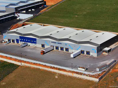 Grey warehouse with loading docks and trucks, beside fields