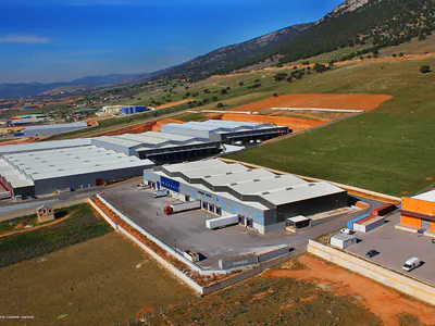 Warehouse complex on a green slope below mountains, aerial view
