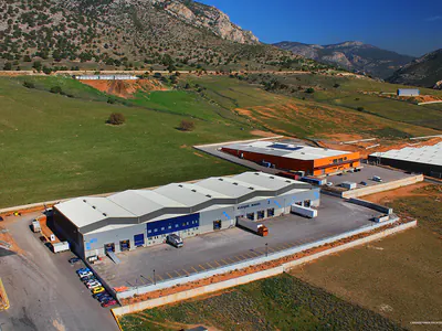 Grey warehouse with blue loading doors and a truck yard, hills behind