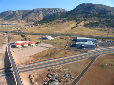Warehouse buildings between a motorway and a railway line, mountains behind, aerial view