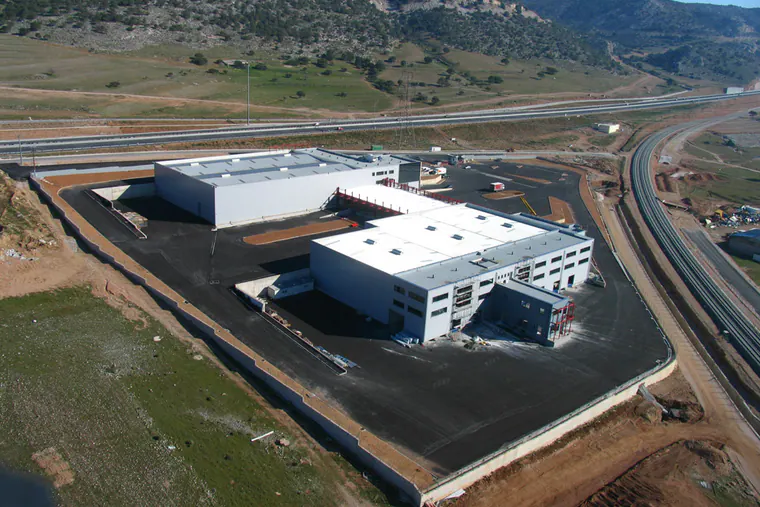 Warehouse and office buildings on an asphalt yard, hills behind