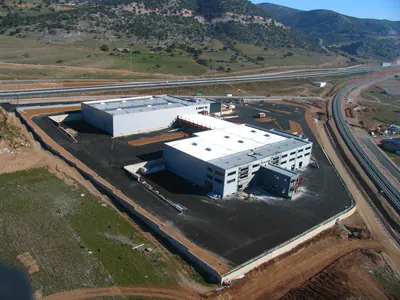 Warehouse and office buildings on an asphalt yard, hills behind