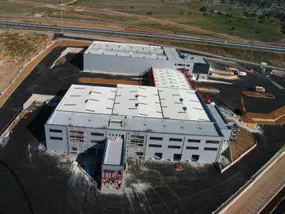 Large warehouse under construction with a red steel frame on its front block, aerial view