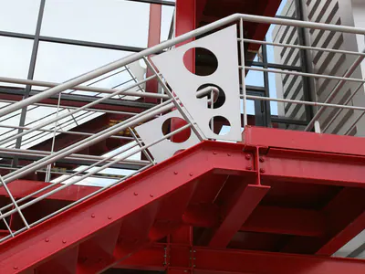 Detail of a red steel staircase with perforated plates in its light grey balustrade