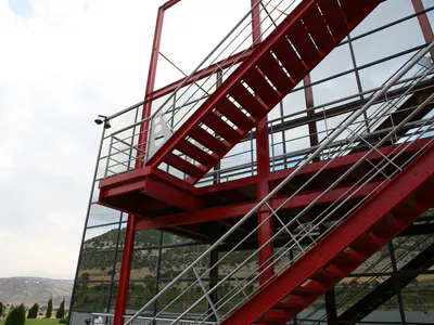 Red steel staircase in a red steel frame in front of a glazed facade, seen from below