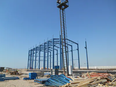 Blue steel portal frames being erected, with a lighting mast