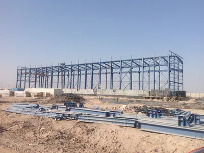 Long blue steel frame of a hall on a desert site, members laid out in front