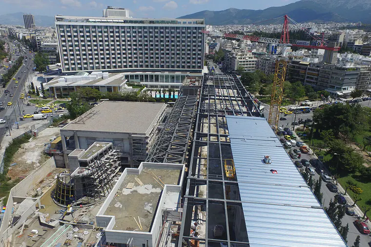 Aerial view of a building under construction with steel roof framing, among city blocks
